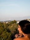 Beautiful young woman in profile looking from a balcony at the horizon with lots of vegetation around her