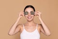 Beautiful young woman putting green tea bags on skin around eyes against beige background Royalty Free Stock Photo