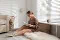 Beautiful young woman reading book near window. Winter atmosphere Royalty Free Stock Photo