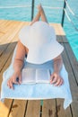Beautiful young woman reading book while relaxing on sun lounger near swimming pool Royalty Free Stock Photo