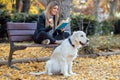 Beautiful young woman reading a book while sitting on bench with her lovely golden retriever dog in the park in autumn Royalty Free Stock Photo