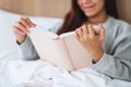 A beautiful young woman reading book in a white cozy bed at home Royalty Free Stock Photo