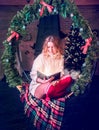 Beautiful young woman is reading a magik book with light sitting on a hanging bench in the Christmas decor. New Year, 2020, Royalty Free Stock Photo