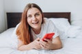 Beautiful young woman reading text message on her mobile phone in the Bed. Check social networks, send sms. The girl is Royalty Free Stock Photo