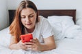 Beautiful young woman reading text message on her mobile phone in the Bed. Check social networks, send sms. The girl is Royalty Free Stock Photo
