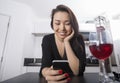 Beautiful young woman reading text message on smart phone at kitchen counter Royalty Free Stock Photo