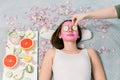 Beautiful young woman receiving spa treatment with pink cosmetic mask, and slices of cucumber on her eyes, skincare Royalty Free Stock Photo