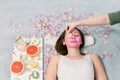 Beautiful young woman receiving spa treatment with pink cosmetic mask, and slices of cucumber on her eyes, skincare Royalty Free Stock Photo