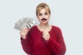 Beautiful young woman in red blouse standing, demonstrate fan of money, holding manlike mustache sticker, looking at camera with