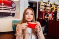 Beautiful young woman with a red cup of coffee at a cafe. Woman drinking hot latte coffee at cozy coffee shop Royalty Free Stock Photo