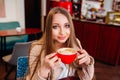 Beautiful young woman with a red cup of coffee at a cafe. Woman drinking hot latte coffee at cozy coffee shop Royalty Free Stock Photo