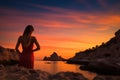 Beautiful young woman in red dress looking at sunset over the sea, Epic red sunset in Cala Llentrisca with model , Ibiza, AI Royalty Free Stock Photo