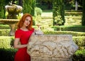 Beautiful young woman with red hair in red dress posing in green summer park. Portrait of beautiful girl in retro style. Pretty Wo Royalty Free Stock Photo