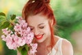 Beautiful young woman with red hair having fun standing in the garden with cherry blossom branch Royalty Free Stock Photo