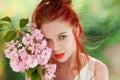 Beautiful young woman with red hair having fun standing in the garden with cherry blossom branch Royalty Free Stock Photo