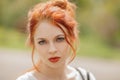 Beautiful young woman with red hair, outside in a park in the sunlight, looking into the camera Royalty Free Stock Photo