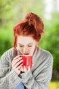 Beautiful young woman with red hair sitting in the garden, relaxing, drinking coffee Royalty Free Stock Photo