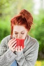 Beautiful young woman with red hair sitting in the garden, relaxing, drinking coffee Royalty Free Stock Photo