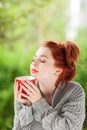 Beautiful young woman with red hair sitting in the garden, relaxing, drinking coffee Royalty Free Stock Photo