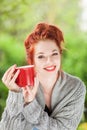 Beautiful young woman with red hair sitting in the garden, relaxing, drinking coffee Royalty Free Stock Photo