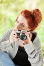 Beautiful young woman with red hair sitting in the garden taking pictures with camera Royalty Free Stock Photo