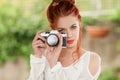 Beautiful young woman with red hair sitting in the garden taking pictures with camera