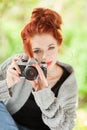 Beautiful young woman with red hair sitting in the garden taking pictures with camera Royalty Free Stock Photo