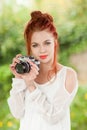 Beautiful young woman with red hair sitting in the garden taking pictures with camera Royalty Free Stock Photo