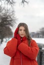 Beautiful young woman in red jacket and knitted mittens sadness look in winter park. Winter portrait of girl Royalty Free Stock Photo