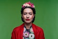 Beautiful young woman with red make up looking like Frida Kahlo. Over green background