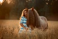 Beautiful young woman with red tinker horse in oats field