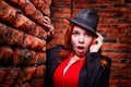 Beautiful young woman with redhair and black hat being near red brick wall inside Royalty Free Stock Photo
