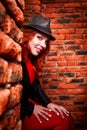 Beautiful young woman with redhair and black hat being near red brick wall inside Royalty Free Stock Photo