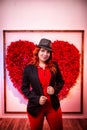 Beautiful young woman with redhair and black hat being near white wall with red heart Royalty Free Stock Photo
