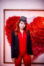 Beautiful young woman with redhair and black hat being near white wall with red heart Royalty Free Stock Photo