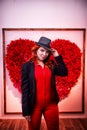 Beautiful young woman with redhair and black hat being near white wall with red heart Royalty Free Stock Photo