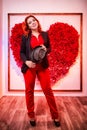 Beautiful young woman with redhair and black hat being near white wall with red heart Royalty Free Stock Photo