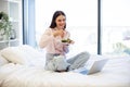 Young woman on bed at home and using modern laptop while eating healthy salad. Royalty Free Stock Photo