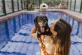 beautiful young woman relaxing in an indoor swimming pool. Cute small sausage dog on her shoulder. Summer time and lifestyle Royalty Free Stock Photo