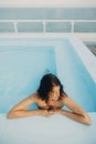 Beautiful young woman relaxing in pool, enjoying warm sunlight and wind. Brunette girl on summer vacation in luxury resort, Royalty Free Stock Photo