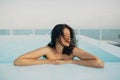 Beautiful young woman relaxing in pool, enjoying warm sunlight and wind. Brunette girl on summer vacation in luxury resort, Royalty Free Stock Photo