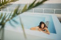 Beautiful young woman relaxing in pool under tropical palm leaves, enjoying day. Brunette girl on vacation in luxury resort, Royalty Free Stock Photo
