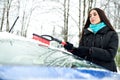 Beautiful young woman removing snow from her car