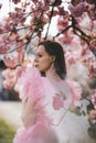 Beautiful young woman in rose dress in blooming sakura garden.