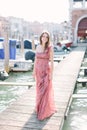 Beautiful young woman in rose dress standing on the background of Venice canal, buildings and gondola. Italy, Europe. Royalty Free Stock Photo