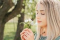 Beautiful young woman`s face close-up woman holding a branch of a flowering tree in her hands and sniffing flowers with her eyes Royalty Free Stock Photo