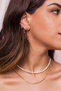 Beautiful young woman`s neck wearing a pearl necklace and a snake chain and gold earings hang from woman`s ear