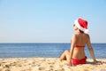 Beautiful young woman in Santa hat and bikini on beach, back view with space for text. Christmas vacation Royalty Free Stock Photo