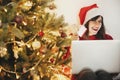 beautiful young woman in santa hat holding credit cards and sitting with laptop at golden beautiful christmas tree with lights Royalty Free Stock Photo