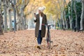 Beautiful young woman sending messages with her smart phone while cycling through the park in autumn Royalty Free Stock Photo